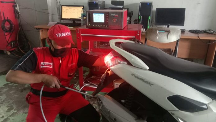 Seorang mekanik bengkel Yamaha sedang melakukan uji emisi pada sebuah sepeda motor.