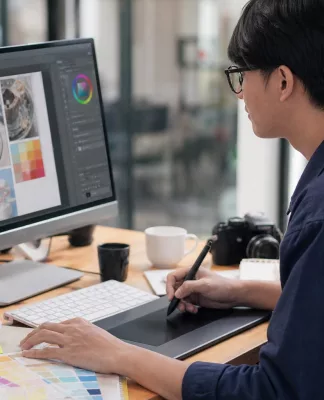 Mengenal Profesi Graphic Designer: Skill yang Wajib Dimiliki Seorang graphic designer bekerja di depan komputer dengan software desain grafis dan tablet digital